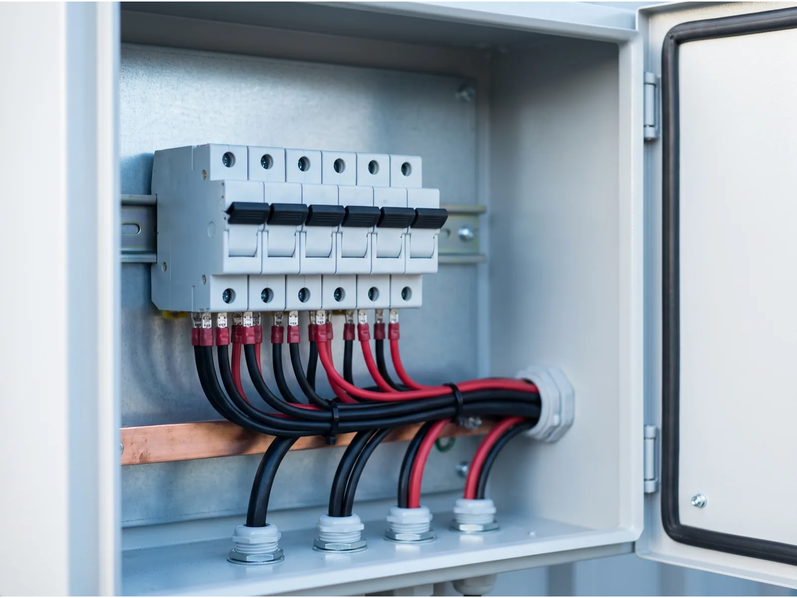 Inside an open DC combiner box: string fuses above dressed red and black cabling and a copper busbar