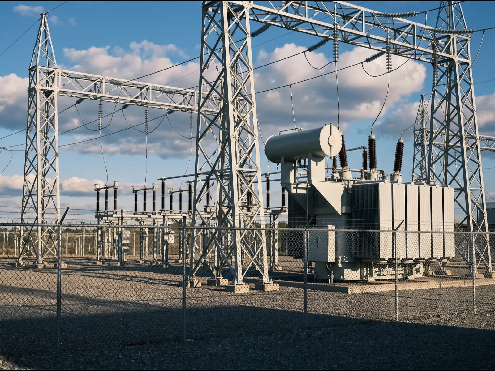 A well-kept distribution substation in directional daylight, lattice structures and a power transformer behind the fence