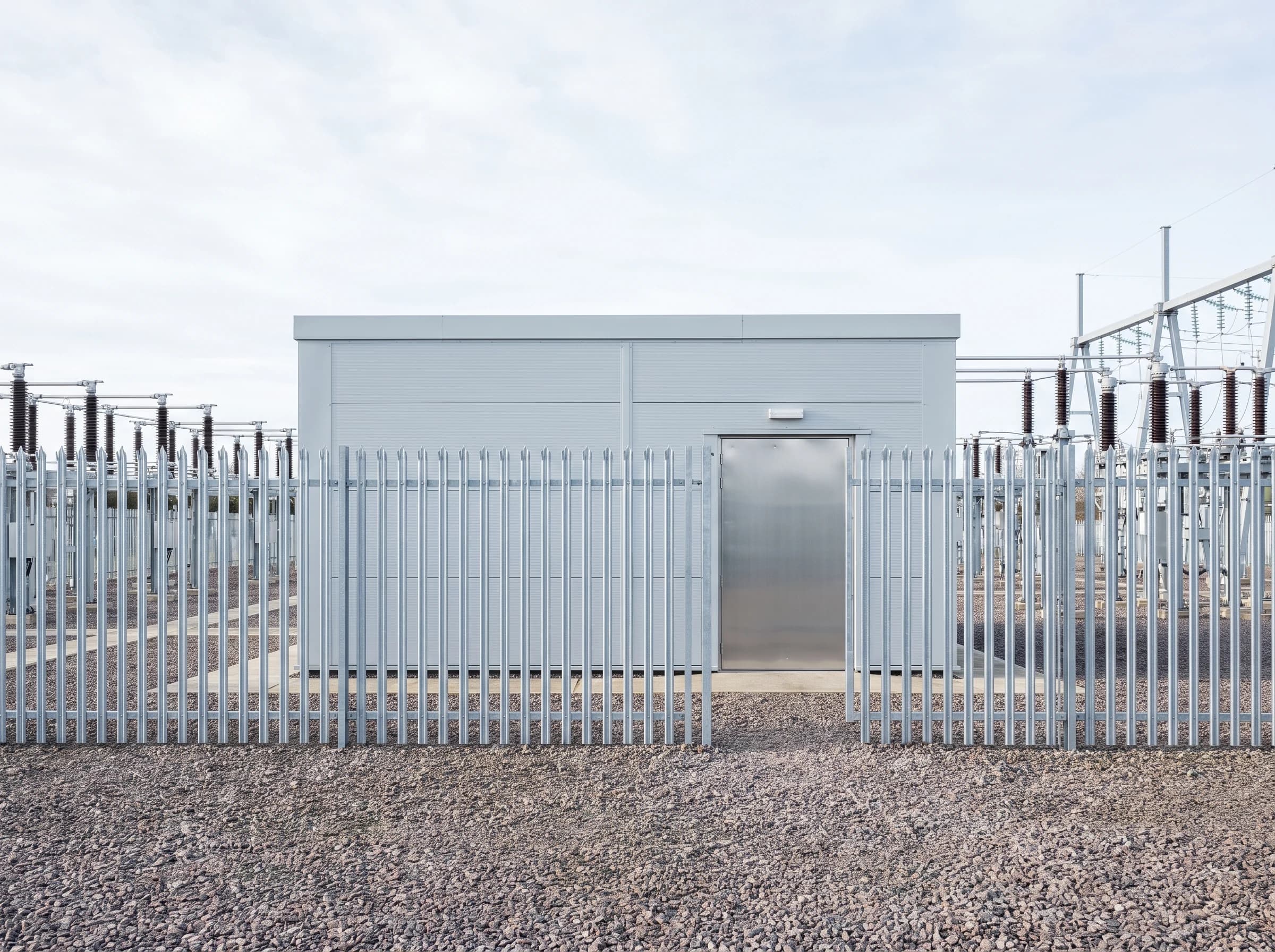A substation control building behind its fence line, with the switchyard beyond