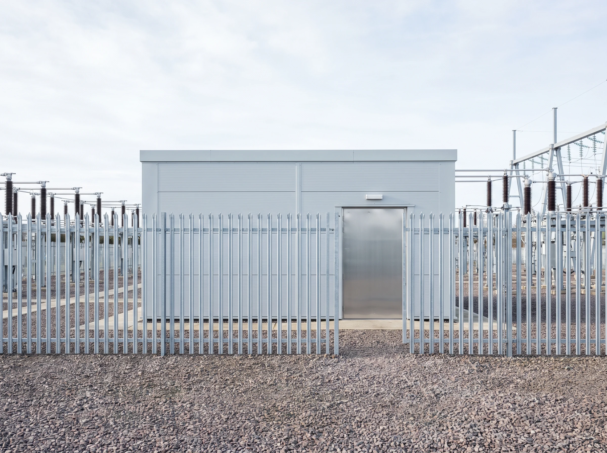 A substation control building behind its fence line, with the switchyard beyond